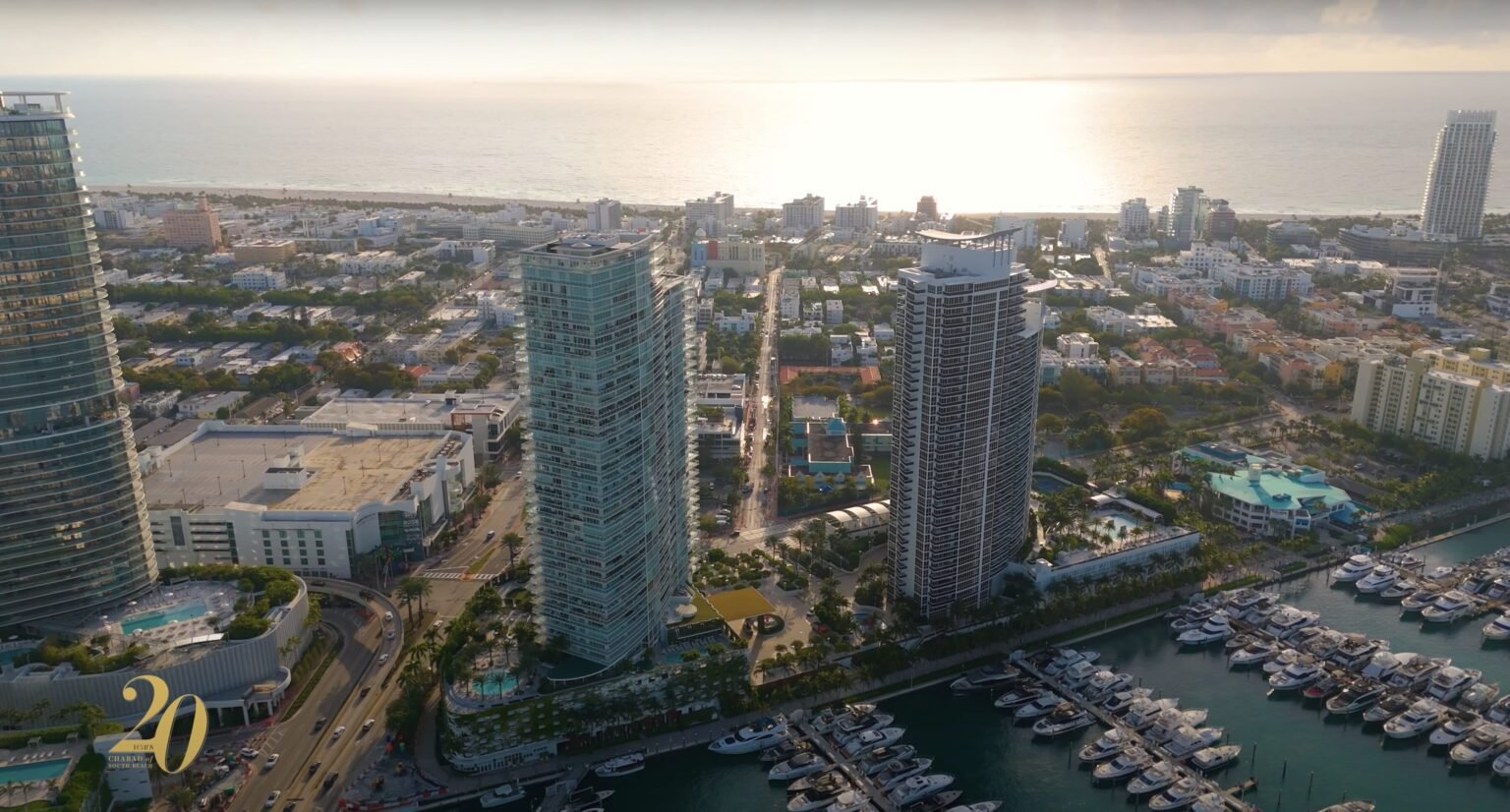 Aerial view of coastal high-rise towers, a marina full of boats and ocean at sunset